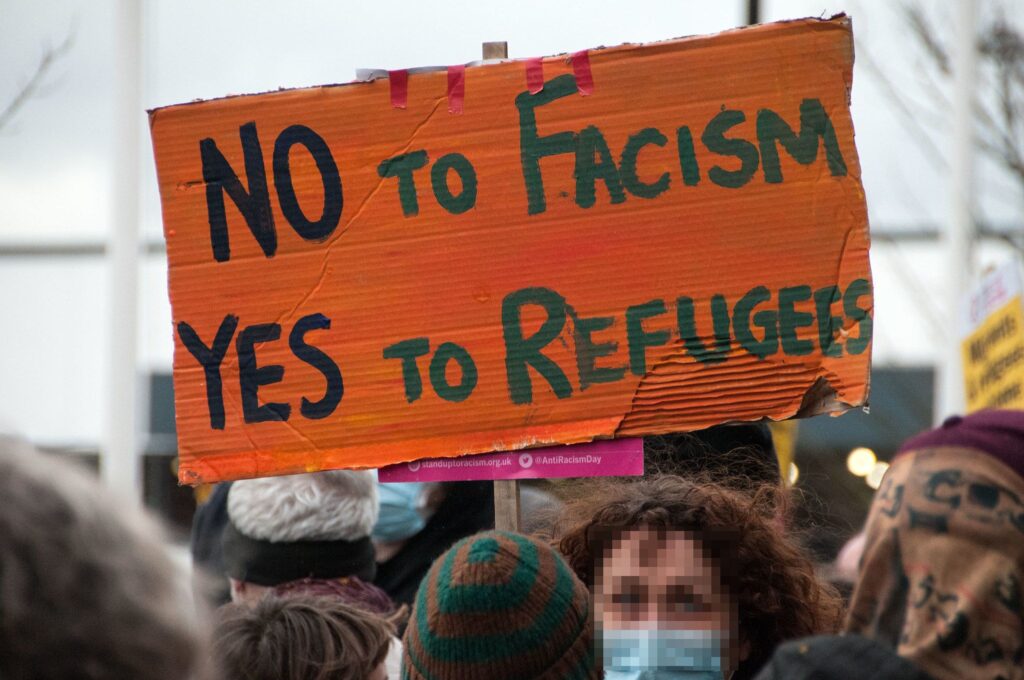 A protestor holds a sign which says "No to [fascism], Yes to Refugees"